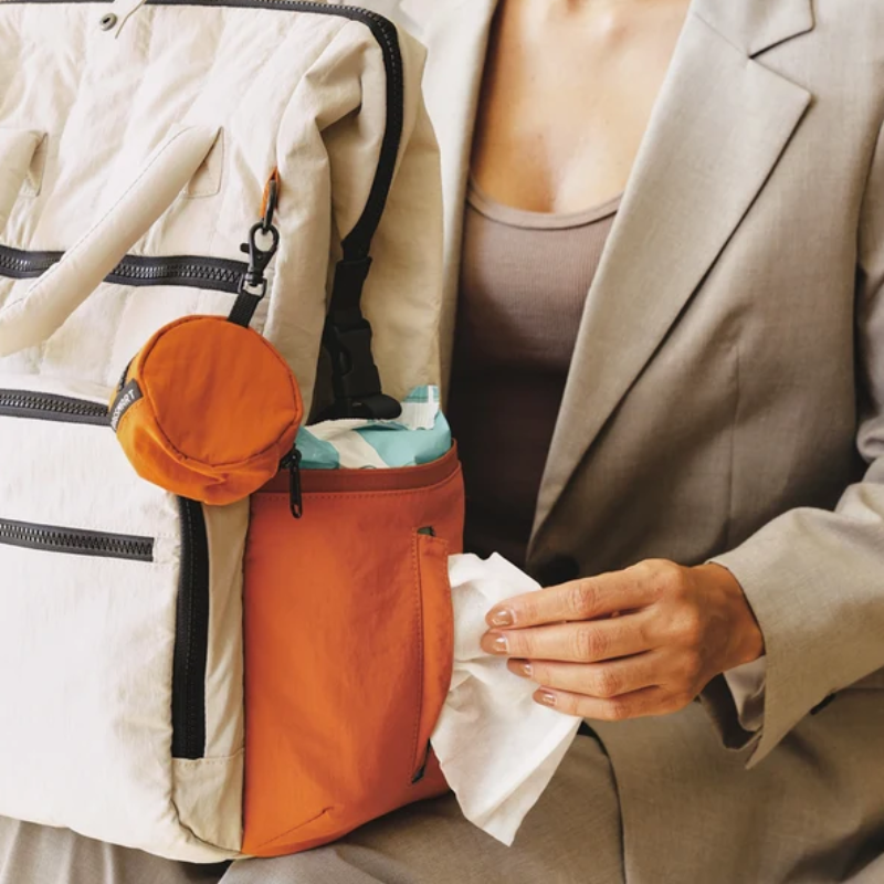 Hand zieht ein Feuchttuch aus dem seitlichen Außenfach des Wickelrucksacks in Creme und Apricot