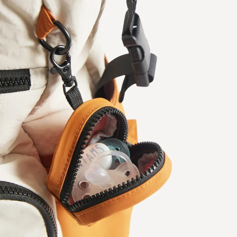 Geöffnete Schnullertasche in Apricot mit zwei Schnullern darin, Nahaufnahme am Wickelrucksack