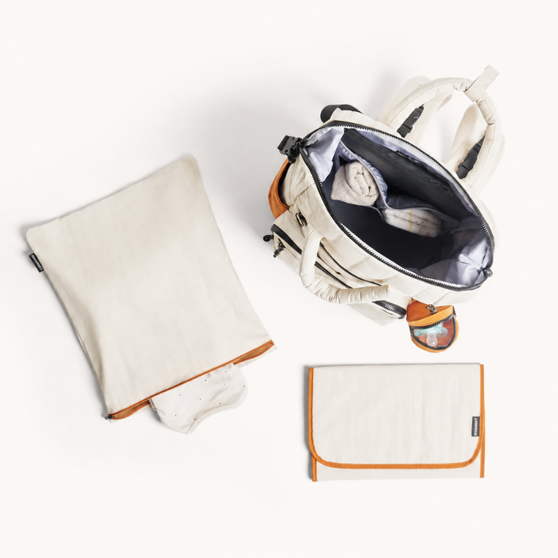 Geöffnete Wickeltasche mit Wickelunterlage und Wäschebeutel daneben, in Creme und Apricot